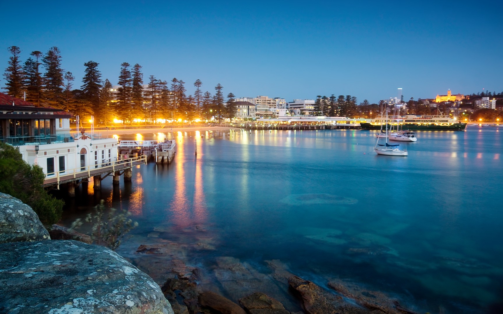 Manly harbour at twilight with warm lights reflecting on calm water